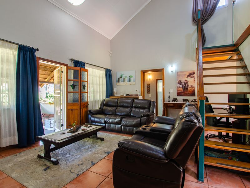 Spacious living room featuring high vaulted ceilings, tiled flooring, and a timber staircase leading to an upper level, with direct access to an outdoor patio.
