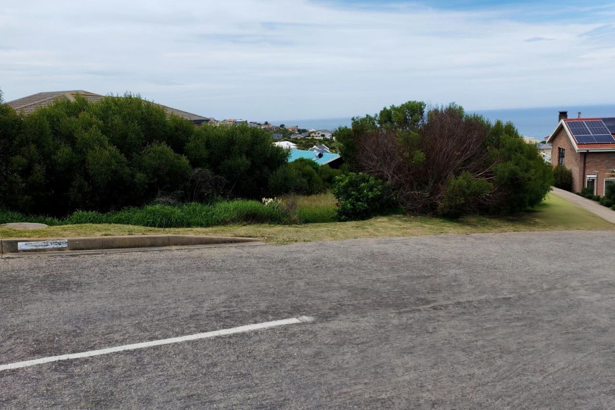 A street-level view of a vacant residential plot featuring established coastal vegetation and a view towards the ocean.