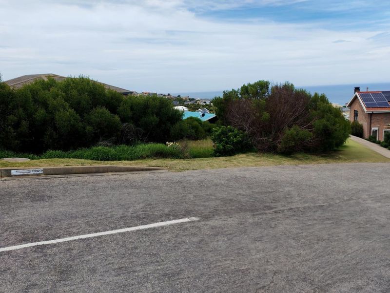 A street-level view of a vacant residential plot featuring established coastal vegetation and a view towards the ocean.