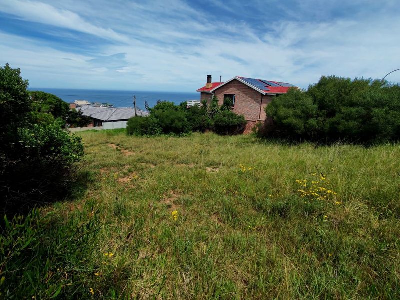A view of a vacant residential plot featuring natural grass coverage and a scenic coastal outlook.