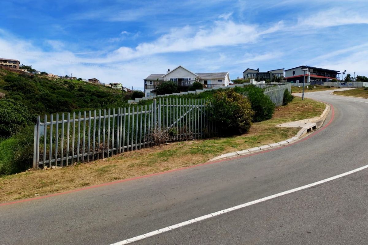A street-level view of a residential property featuring metal palisade fencing along the roadside boundary with paved asphalt road and concrete curbing.
