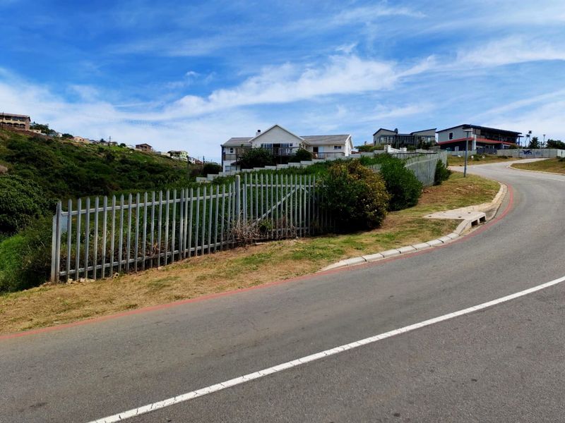 A street-level view of a residential property featuring metal palisade fencing along the roadside boundary with paved asphalt road and concrete curbing.