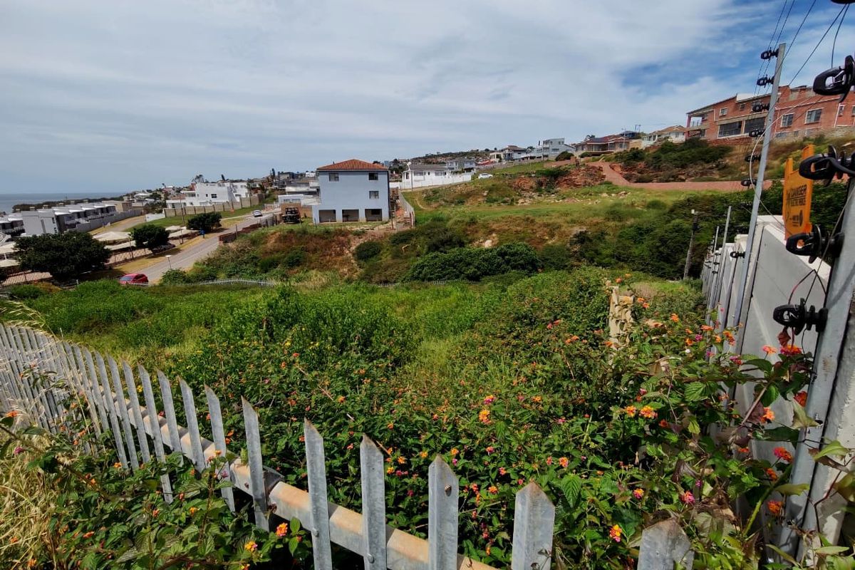 A view of a sloped, undeveloped residential plot featuring established vegetation, enclosed by metal palisade fencing and electric security wiring.