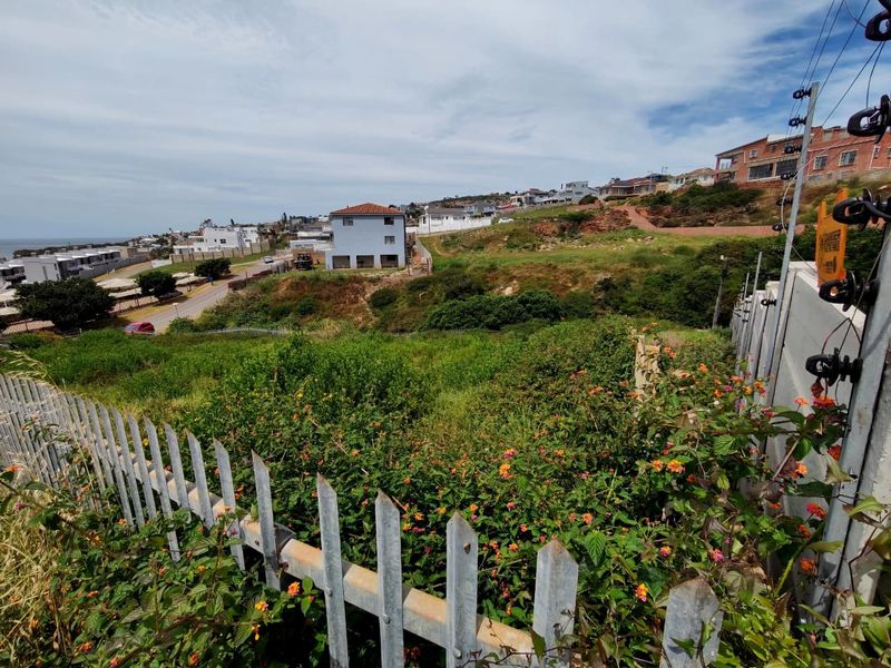 A view of a sloped, undeveloped residential plot featuring established vegetation, enclosed by metal palisade fencing and electric security wiring.
