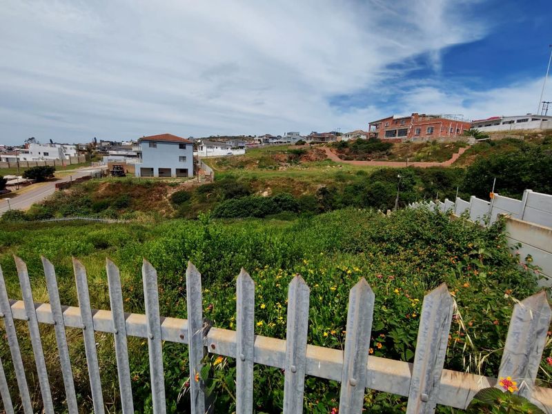 A view of a vacant residential plot featuring metal palisade fencing and natural sloped terrain in an established neighborhood.