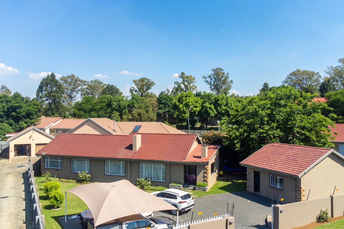Aerial view of a residential property featuring a main house with a tiled roof, paved driveway, detached garage, and secure perimeter walling.
