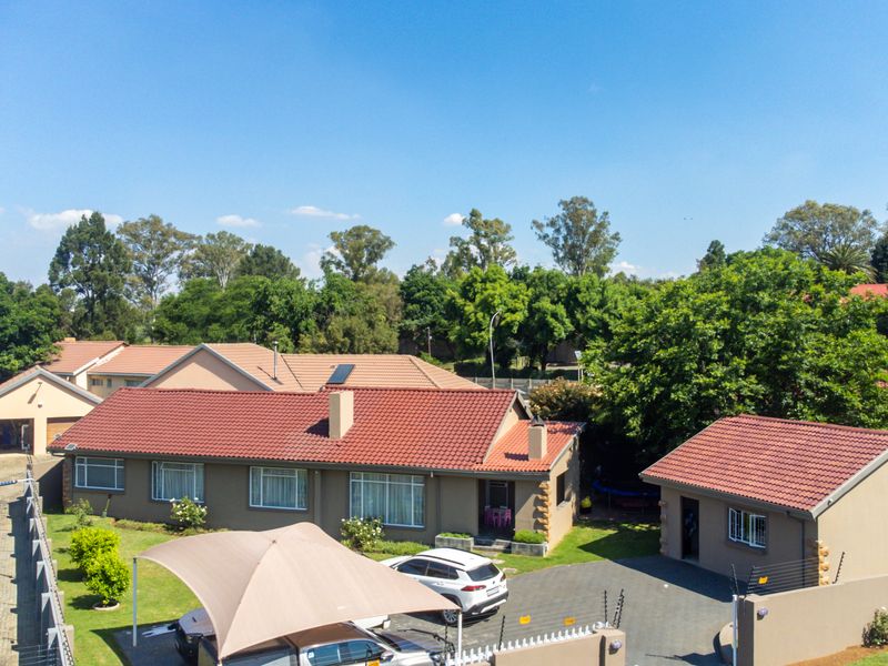 Aerial view of a residential property featuring a main house with a tiled roof, paved driveway, detached garage, and secure perimeter walling.
