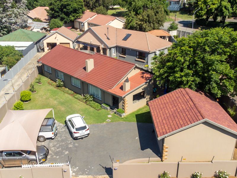 Aerial view of the property featuring a main house with a tiled roof, a detached garage, paved driveway, and secure perimeter walling with electric fencing.