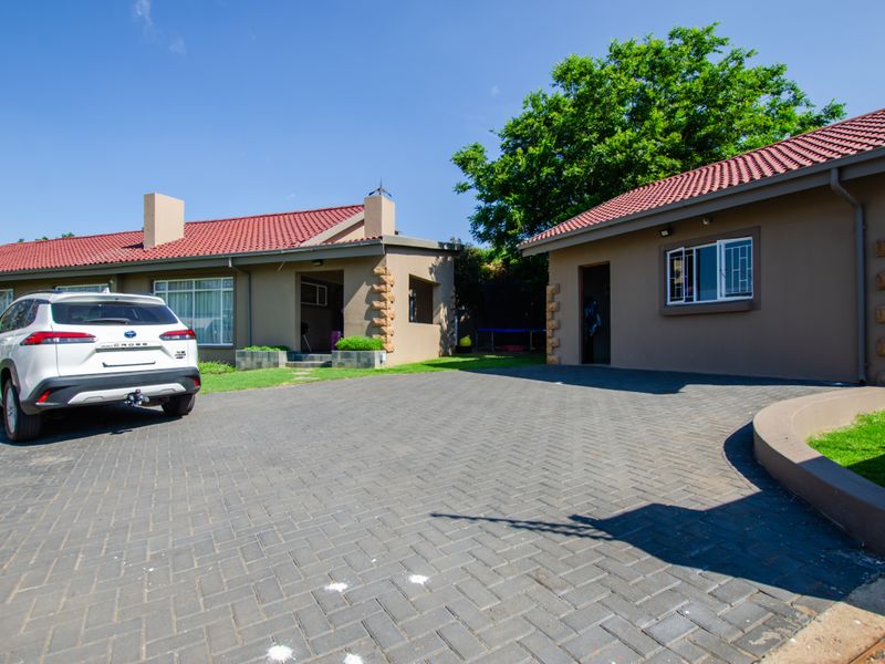 Front exterior view of the house featuring a paved driveway, stone-clad accents, and a tiled roof with well-maintained building facades.