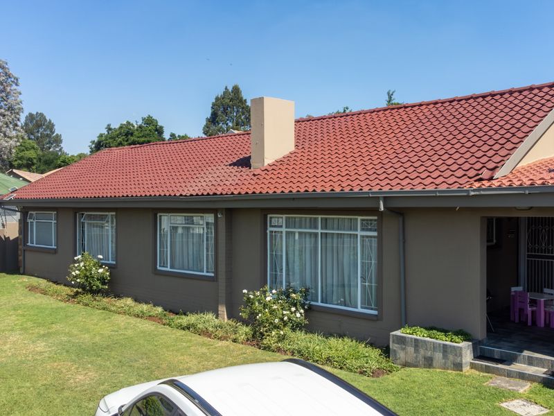 A well-maintained rear elevation of a house featuring a red tiled roof, chimney, and a landscaped garden with a stone-clad planter box.
