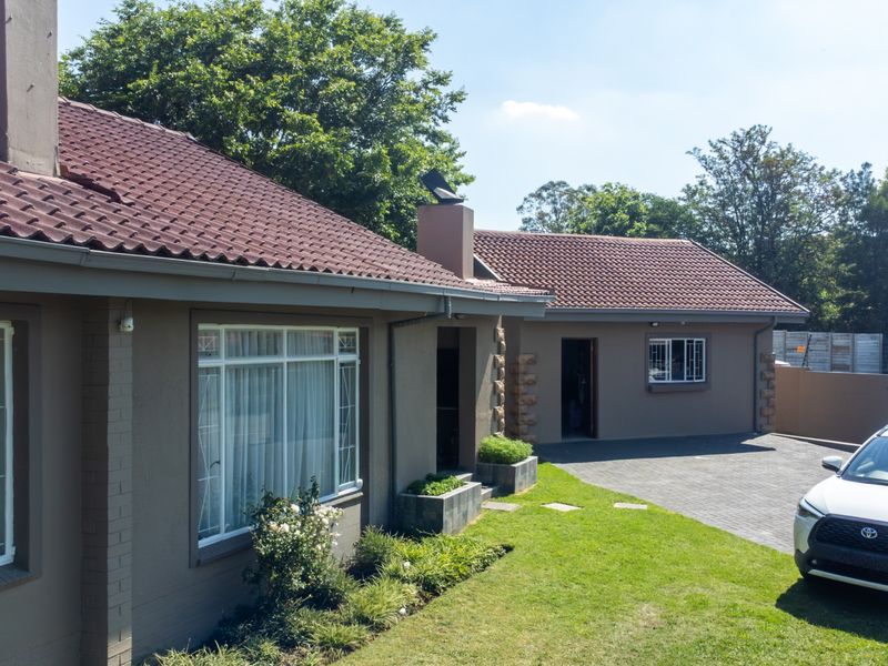 A well-maintained single-story house featuring a tiled roof, brick exterior, paved driveway, and integrated garden planters.