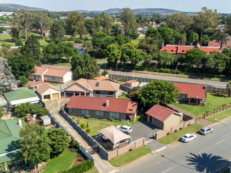 Aerial view of the residential property showing the main house, detached garage, paved driveway, carport, and surrounding garden area within the neighborhood.