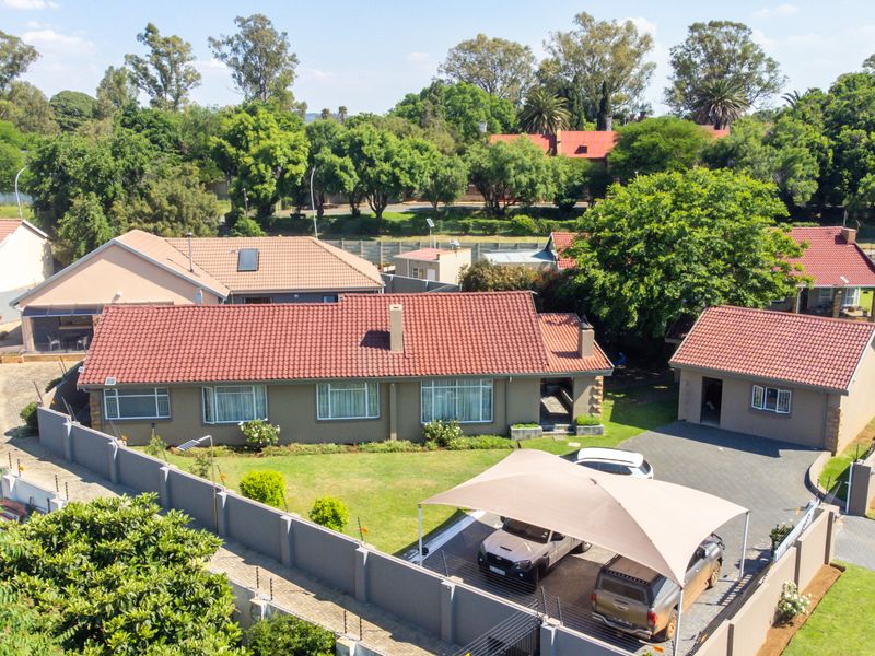 Aerial view of a residential property featuring a main house with a tiled roof, a detached garage, a paved driveway, and a shade sail carport.