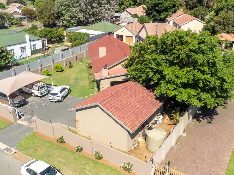 Aerial view of the property featuring a tiled roof house, paved driveway, shade cloth carport, perimeter wall with electric fencing, and a water storage tank.