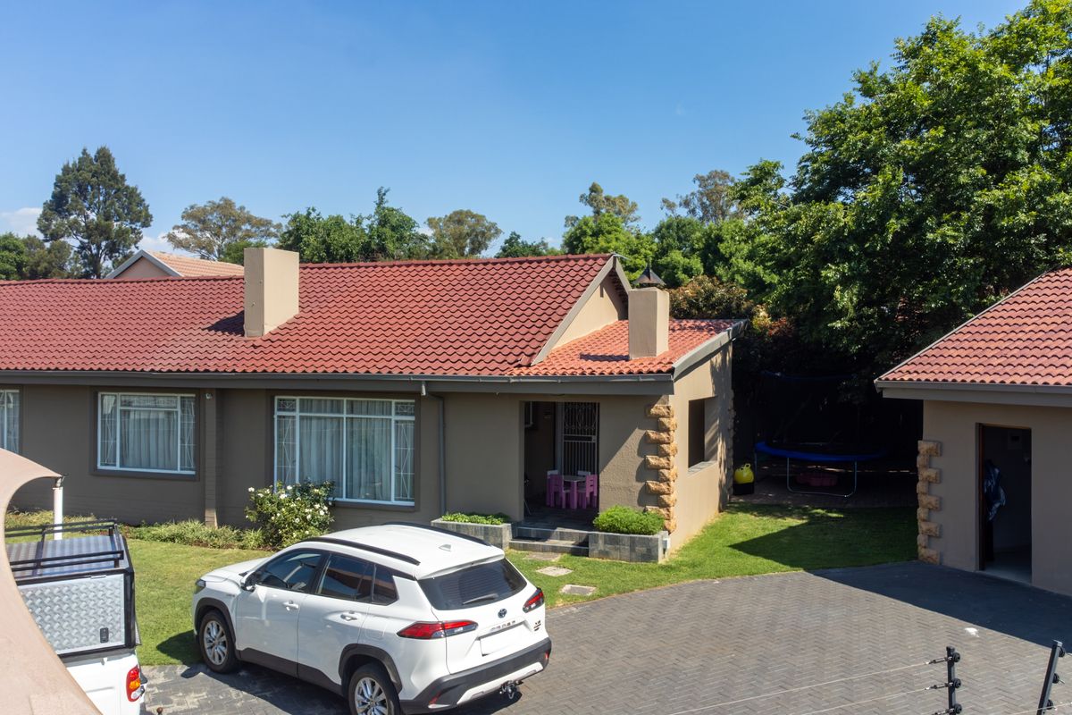Rear view of the property featuring a tiled roof, paved driveway, and secure perimeter fencing with stone-clad architectural accents.