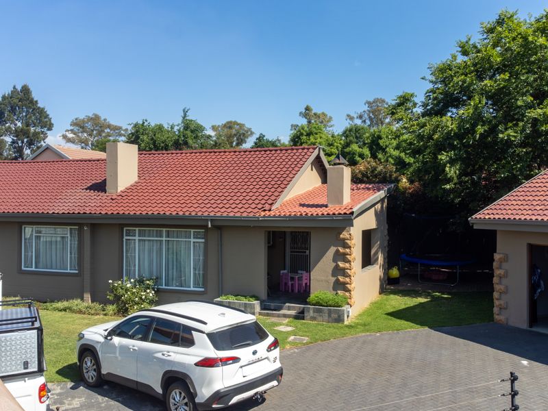 Rear view of the property featuring a tiled roof, paved driveway, and secure perimeter fencing with stone-clad architectural accents.