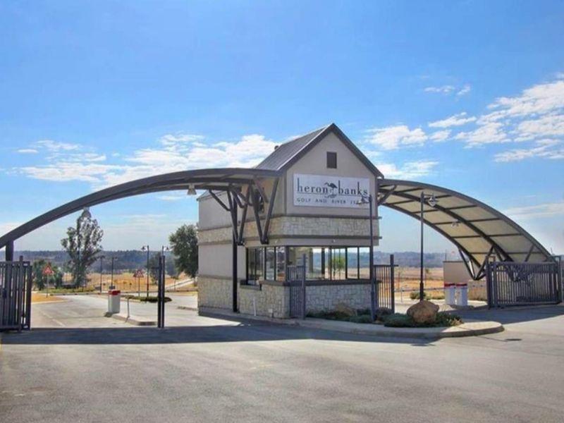 The secure entrance gatehouse of Heron Banks Golf and River Estate, featuring a modern metal archway and stone-clad guardhouse.