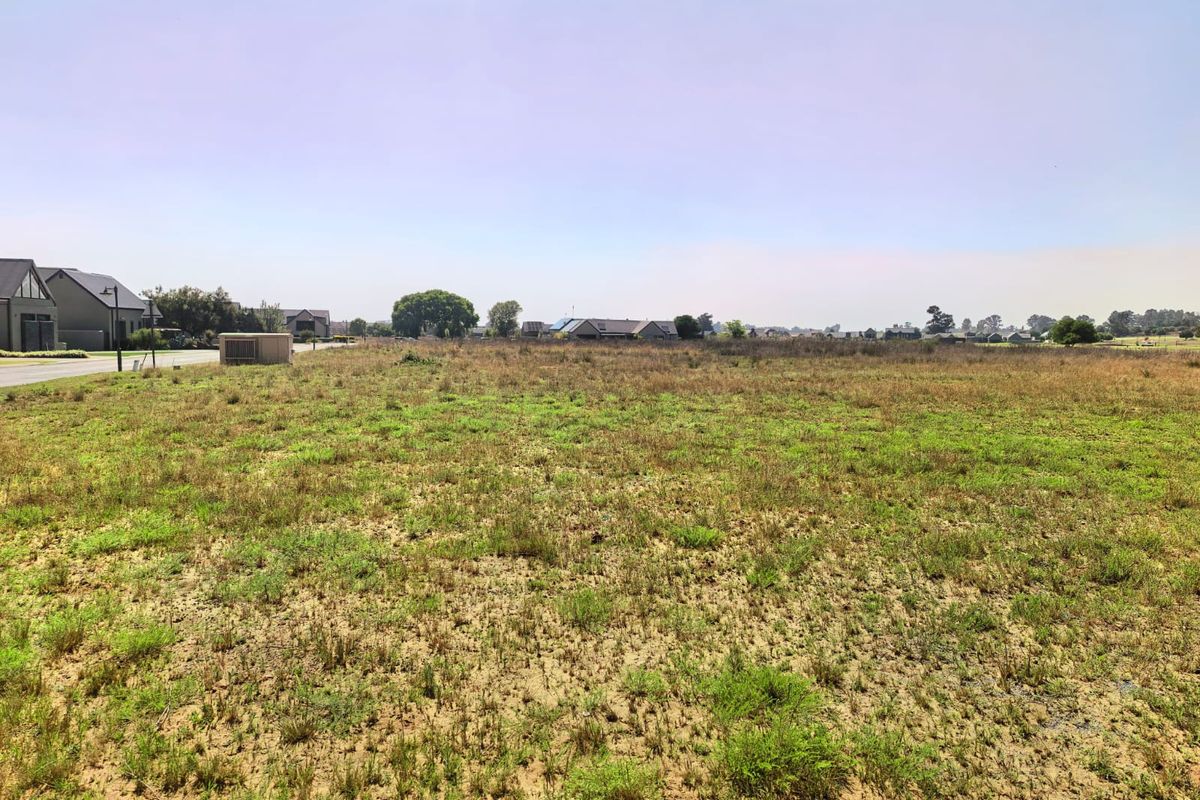 A wide-angle view of a vacant residential plot of land, showing the level terrain and surrounding neighborhood context.