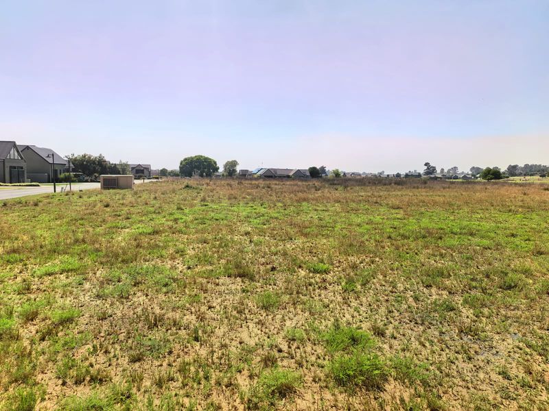 A wide-angle view of a vacant residential plot of land, showing the level terrain and surrounding neighborhood context.