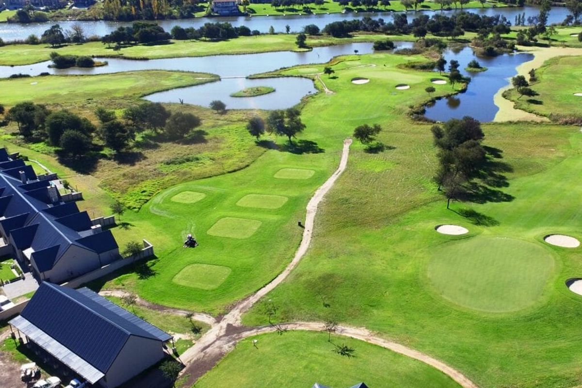 An aerial view of a residential property situated adjacent to a golf course with scenic water features and surrounding landscape.