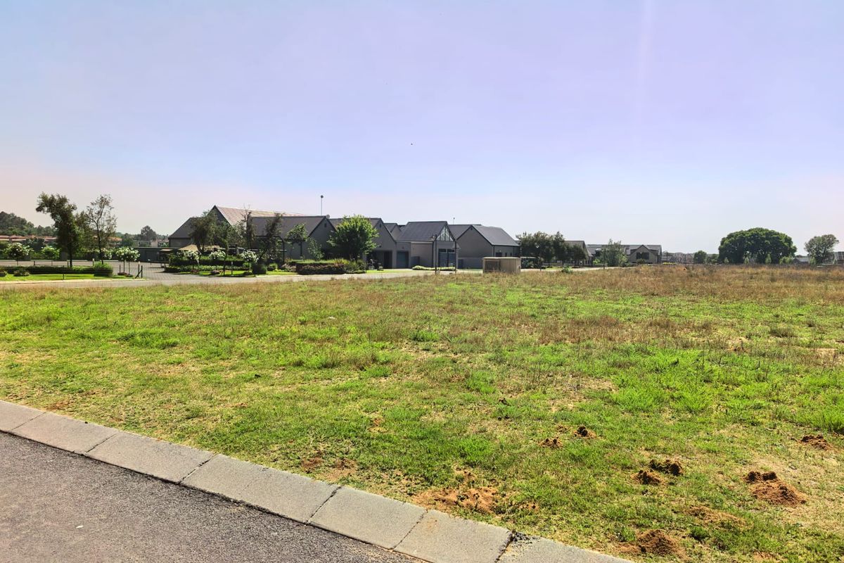 A vacant residential plot of land featuring grassed terrain and a paved curb, situated in a developed estate setting.
