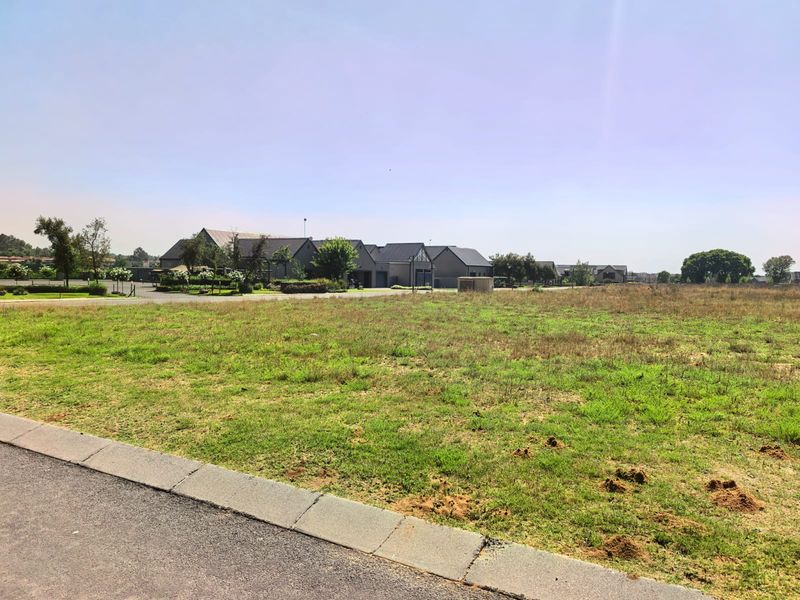 A vacant residential plot of land featuring grassed terrain and a paved curb, situated in a developed estate setting.