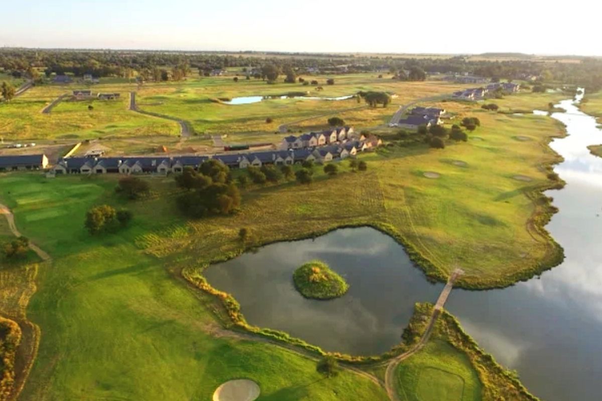 An aerial view of a residential estate featuring expansive green golf course fairways, landscaped lakes, and surrounding natural terrain.