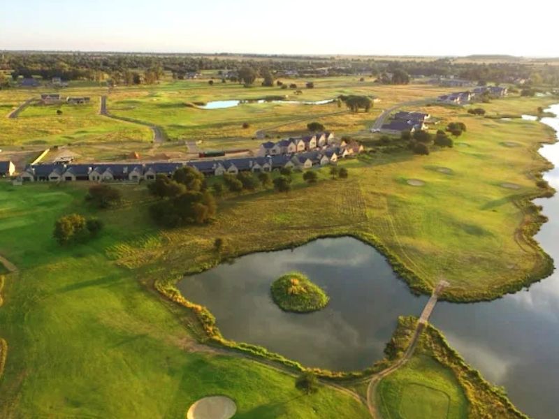 An aerial view of a residential estate featuring expansive green golf course fairways, landscaped lakes, and surrounding natural terrain.