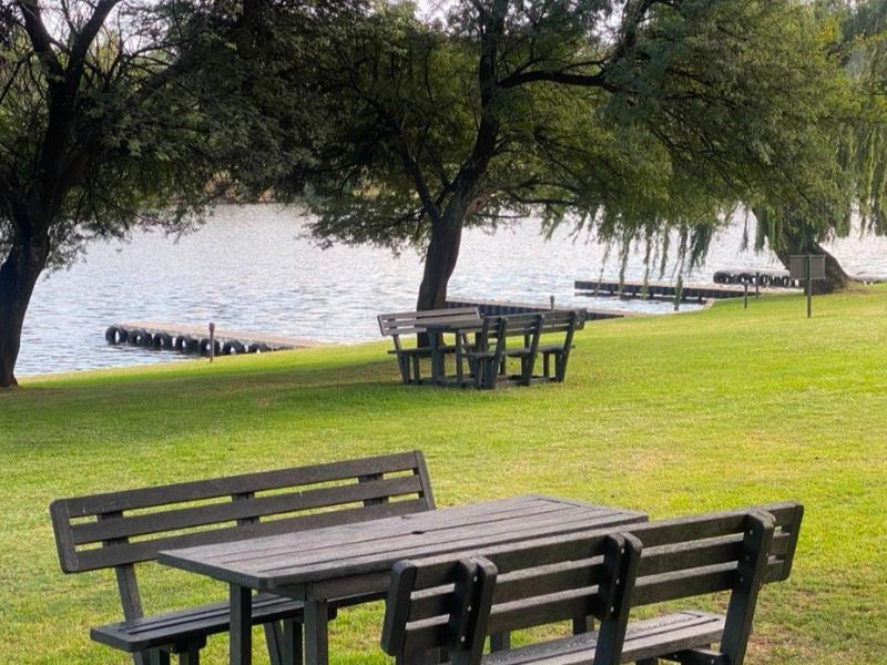 A scenic waterfront garden area featuring well-maintained lawn, mature trees, and direct access to the water with jetty infrastructure.