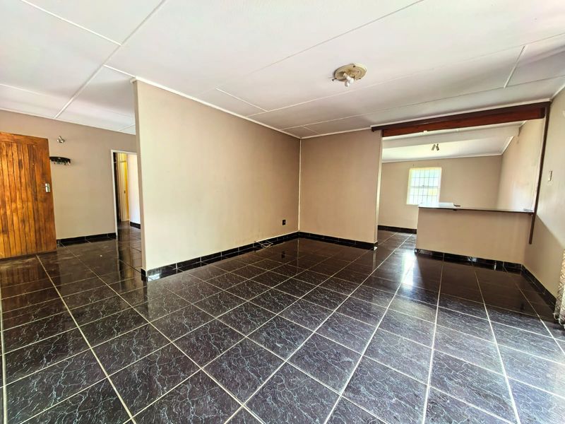 Spacious open-plan living area featuring dark marble-effect floor tiles, a built-in breakfast bar, and neutral wall tones, offering a blank canvas for renovation.