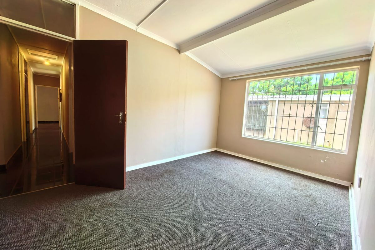 An empty bedroom featuring carpeted flooring, a sloped ceiling, and security bars on the window, offering a blank canvas for potential updates.