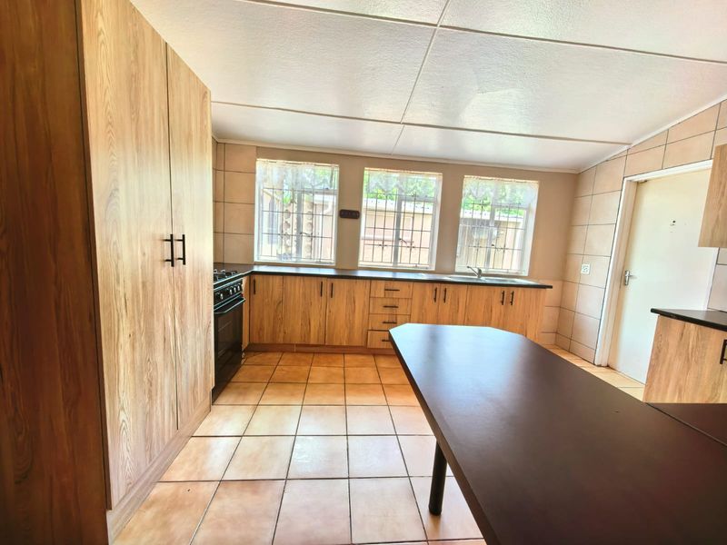 A functional kitchen featuring wood-look cabinetry, tiled surfaces, a freestanding stove, and ample natural light through windows with security bars.