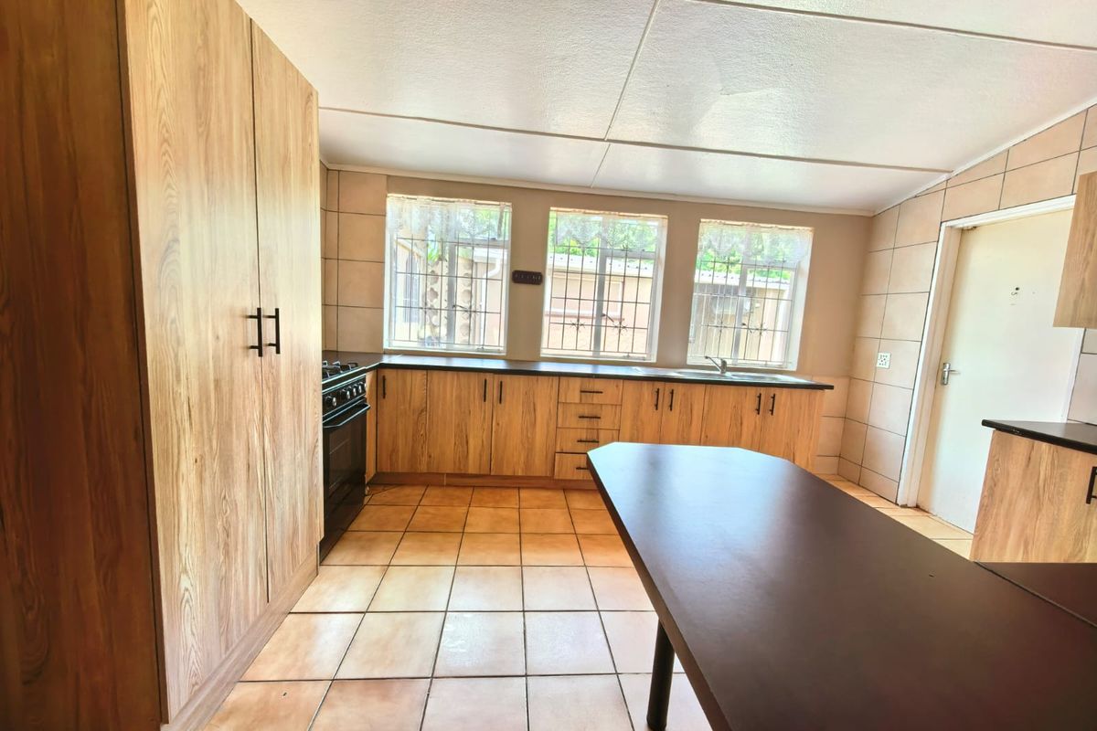 A functional kitchen featuring wood-look cabinetry, tiled surfaces, a freestanding stove, and ample natural light through windows with security bars.