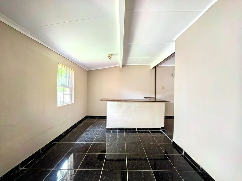 An empty living area featuring dark tiled flooring and a built-in bar counter, offering a versatile space for customization.