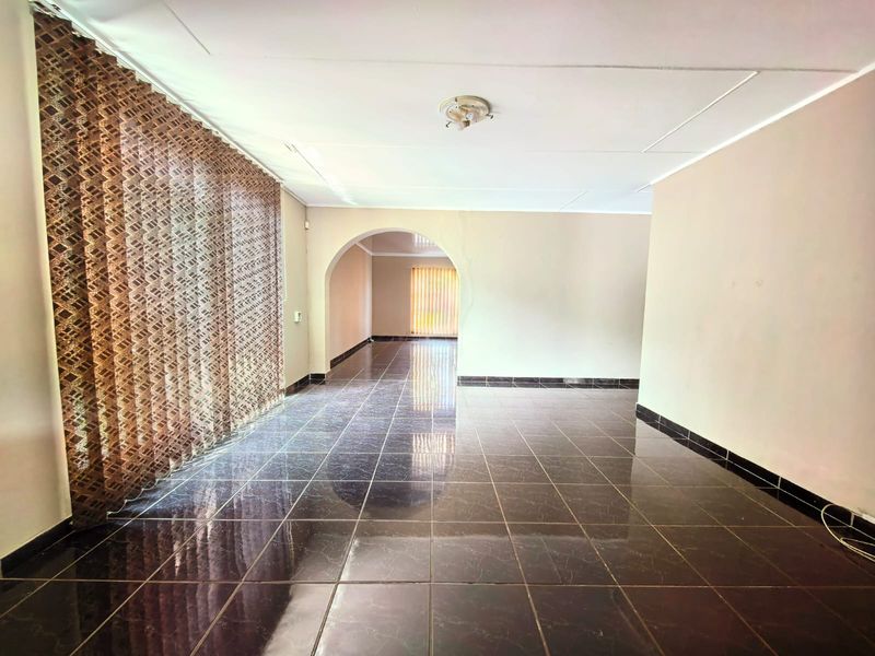 An empty living area featuring dark tiled flooring, a central archway, and vertical blinds, offering a blank canvas for interior design.