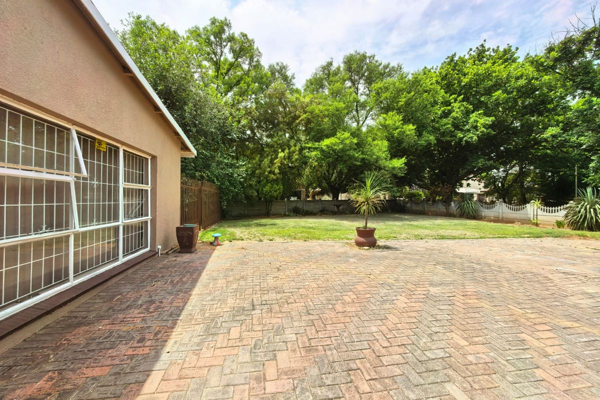 Spacious rear garden featuring a large brick-paved patio area, established trees, and secure perimeter fencing.