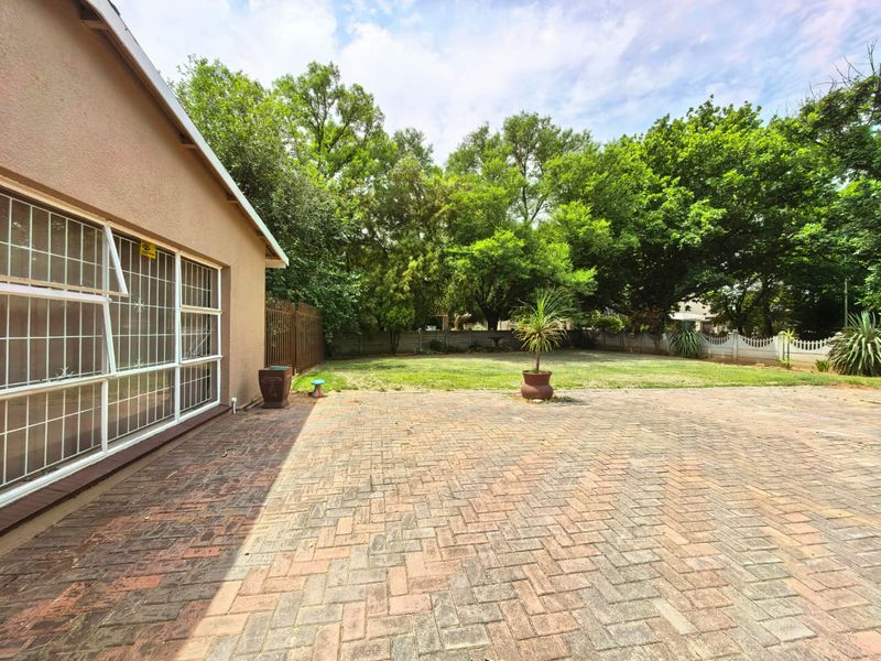 Spacious rear garden featuring a large brick-paved patio area, established trees, and secure perimeter fencing.