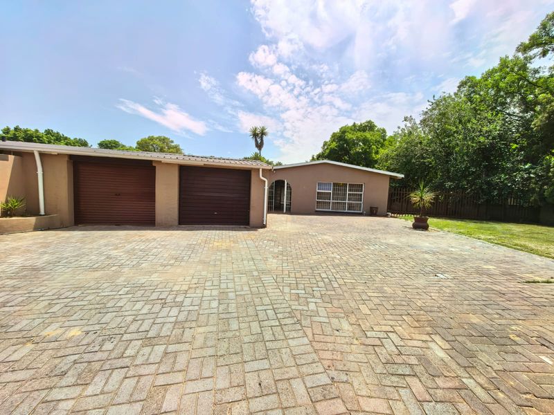 Front exterior view of a single-story house featuring a double garage, extensive paved driveway, and secure entrance gate.