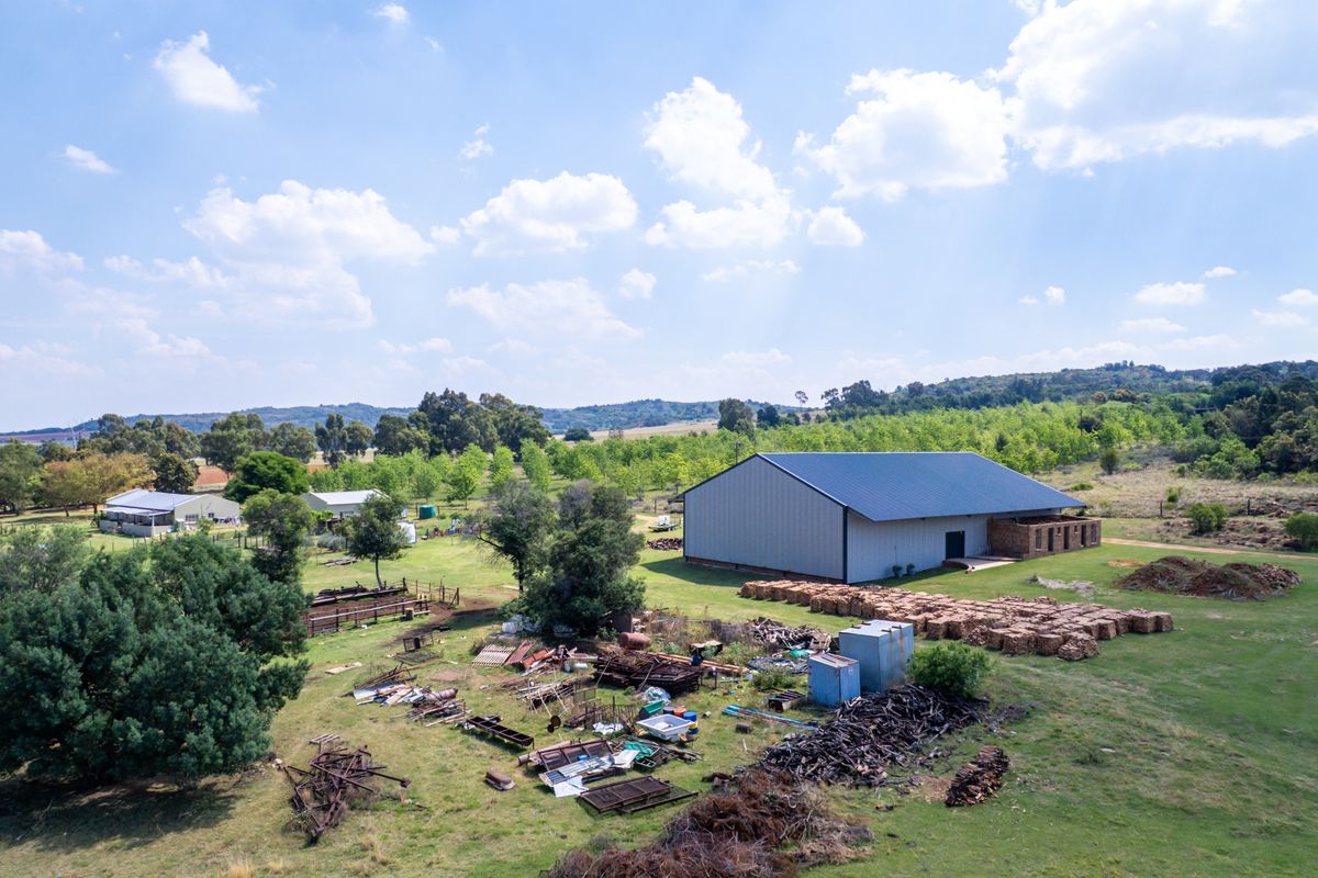 Aerial view of a farm property featuring a large metal shed, outbuildings, and extensive pasture land with some scattered debris.