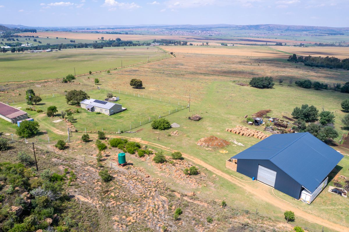 Aerial view of a farm property featuring a large metal shed, residential dwelling with solar panels, water storage, and expansive surrounding agricultural land.