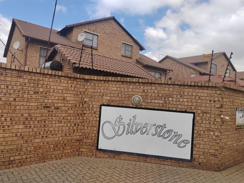 Exterior view of the Silverstone apartment complex entrance, featuring a face brick boundary wall, paved driveway, and tiled roof architecture.