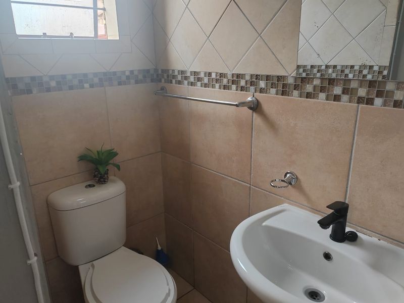 A compact bathroom featuring neutral ceramic wall tiles with a decorative mosaic border, a modern black basin mixer, and a standard toilet.