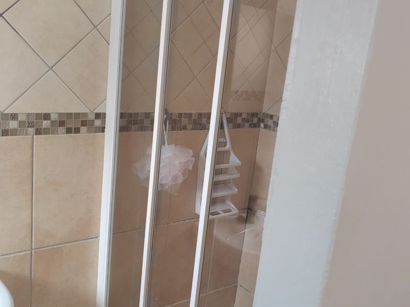 A functional bathroom shower enclosure featuring neutral wall tiles with a decorative mosaic border and a tiled floor.
