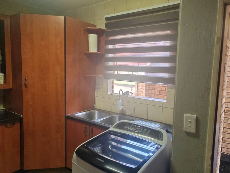 A functional laundry area featuring built-in wooden cabinetry, a double sink, and tiled backsplash, providing practical utility space.