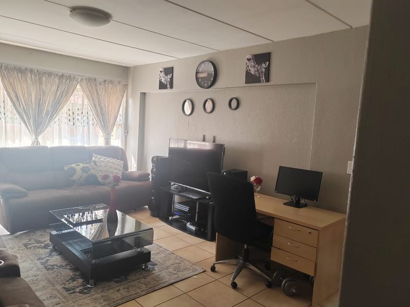 A living room area featuring tiled flooring and a drop ceiling, providing a functional space for relaxation and home office use.