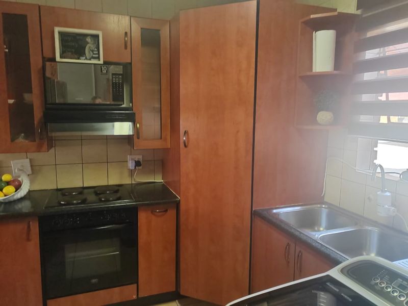 A functional kitchen featuring wood-finish cabinetry, integrated appliances including an oven and hob, and a double stainless steel sink with tiled backsplash.