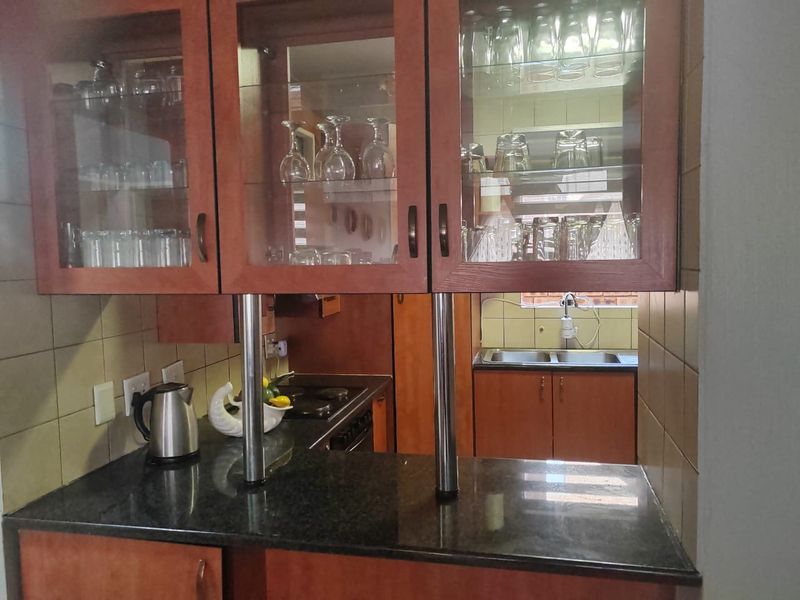 A functional kitchen featuring granite countertops, wooden cabinetry with glass-front display units, and a double stainless steel sink with a tiled backsplash.