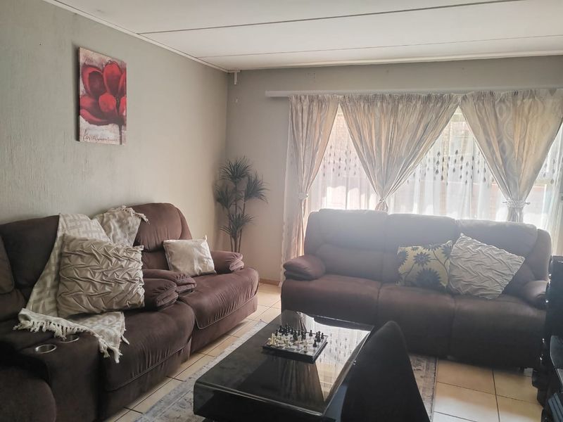 A comfortable living room featuring tiled flooring and large windows with installed curtain tracks, providing a functional and well-lit space.