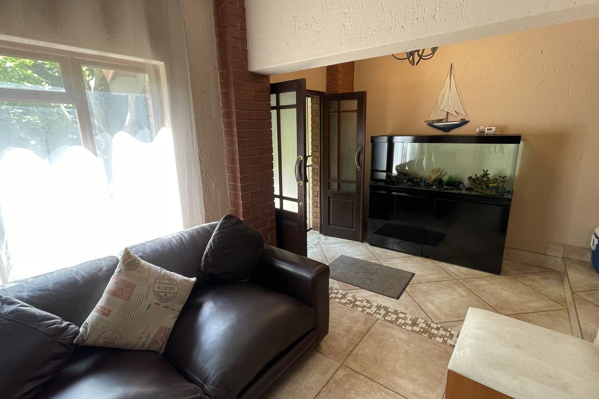 A living area featuring tiled floors, exposed brick detailing, and timber-framed glass doors leading to an adjacent space.