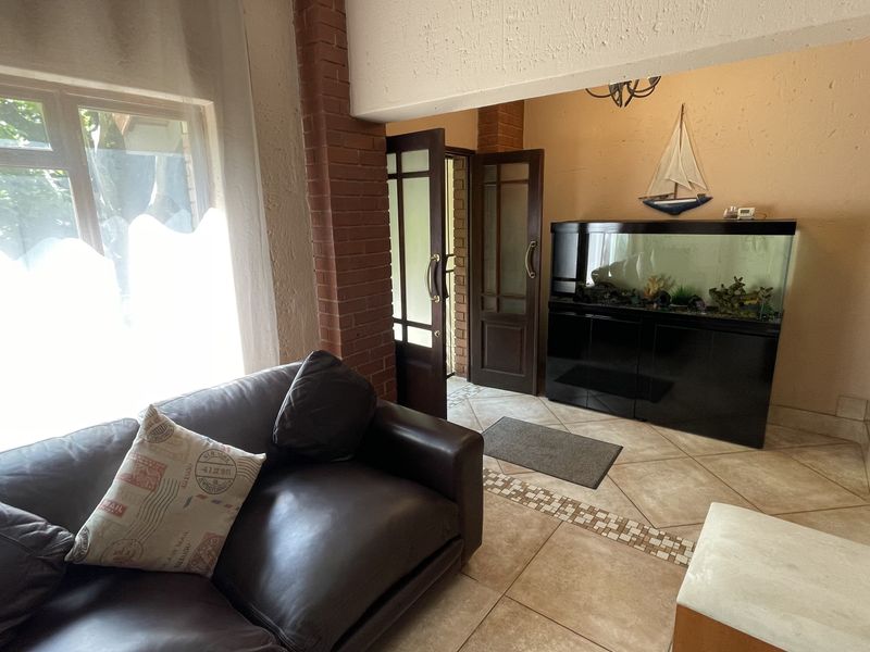 A living area featuring tiled floors, exposed brick detailing, and timber-framed glass doors leading to an adjacent space.
